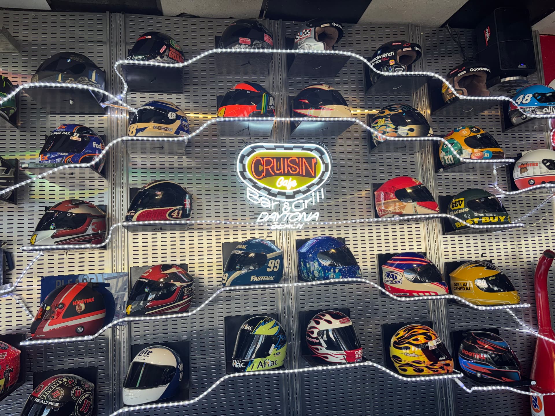 Neon Cruisin Café sign inside a light-up race car outline surrounded by champion racing helmets